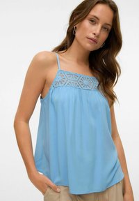 Jasnoniebieska, bezrękawnik z koronkowymi detalami przy dekolcie, zwiewny materiał i cienkie ramiączka. Miękka faktura i luźny krój.