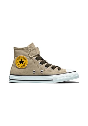 Basket Converse montante beige avec lacets noirs, écusson logo rond jaune, bout blanc et semelle blanche rayée de noir.