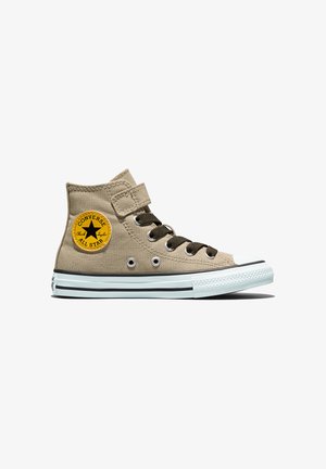 Basket Converse montante beige avec lacets noirs, écusson logo rond jaune, bout blanc et semelle blanche rayée de noir.