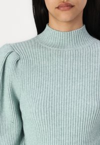 Light blue ribbed knit sweater with a high collar and puffed shoulders, showcasing a smooth texture and form-fitting design.