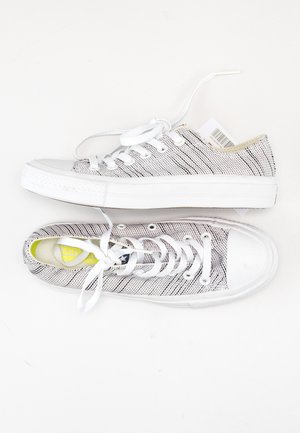 Białe tenisówki na płótnie z teksturowanym czarno-białym wzorem, białe sznurowadła i gumowe podeszwy. Zawierają żółty detal wkładki.