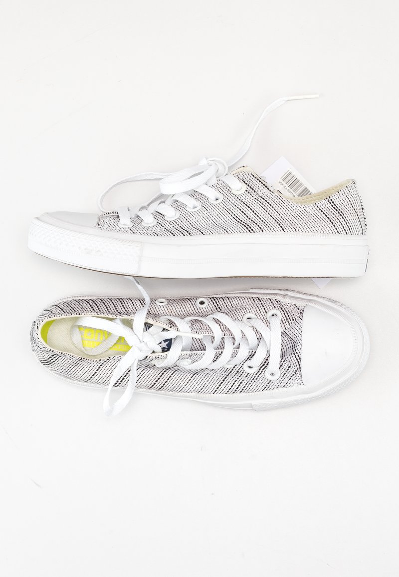 Zapatillas de lona blancas con un patrón texturizado en blanco y negro, cordones blancos y suelas de goma. Incluyen un detalle de plantilla amarilla.