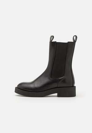 Bottines Chelsea en cuir noir avec des panneaux latéraux élastiques, des languettes de tirage, un bout rond et une semelle en caoutchouc noir épaisse, offrant une texture lisse.