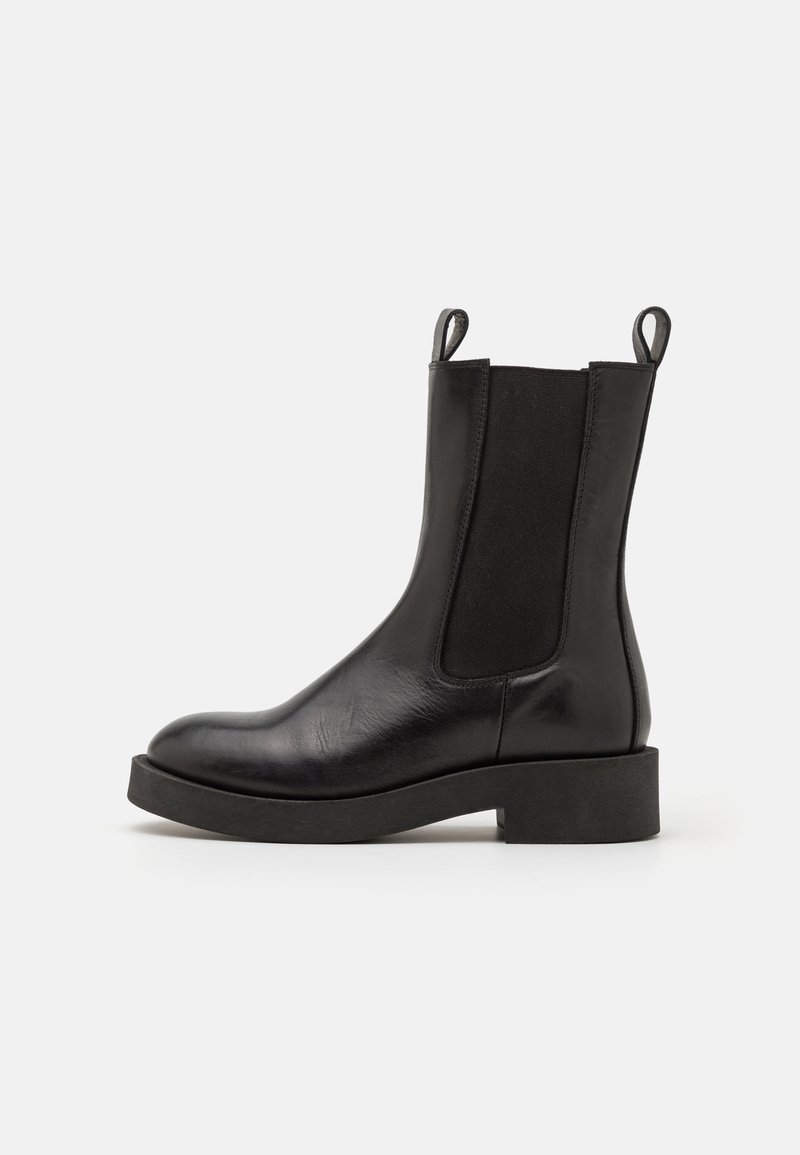 Bottines Chelsea en cuir noir avec des panneaux latéraux élastiques, des languettes de tirage, un bout rond et une semelle en caoutchouc noir épaisse, offrant une texture lisse.