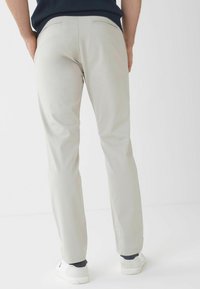 Pantaloni grigio chiaro in tessuto liscio, con taglio a gamba dritta e due tasche posteriori, abbinati a sneaker bianche.