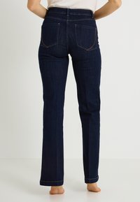 Vaqueros de mezclilla azul oscuro con corte recto, que cuentan con dos bolsillos traseros y detalles mínimos de costura en la pretina y los bajos.