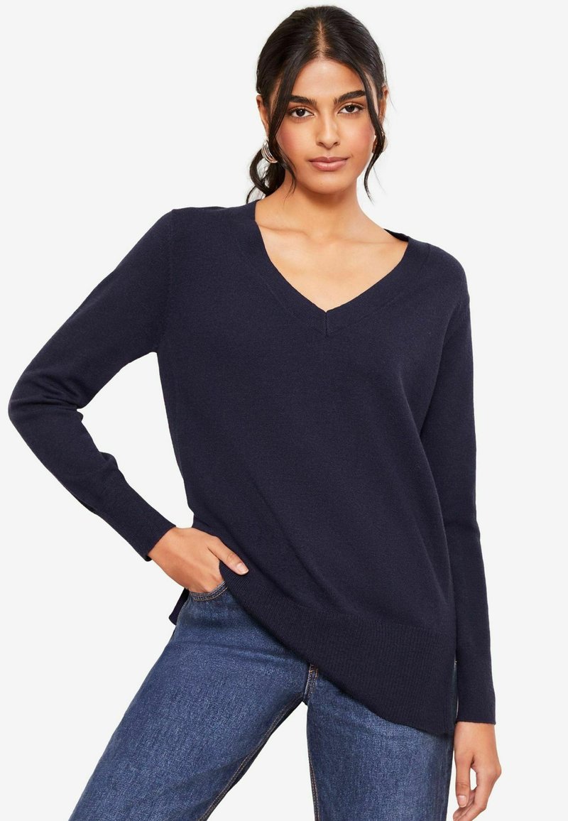 Granatowy sweter z dekoltem w serek, z długimi rękawami, ściągaczem na dole i luźnym fasonem, wykonany z miękkiego materiału, w zestawie z dżinsami.