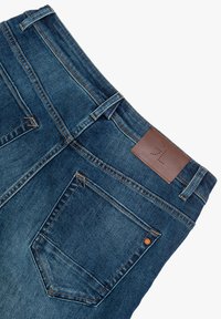 Jeans in denim con un lavaggio blu scuro, caratterizzati da una toppa in pelle marrone in vita, due tasche posteriori e dettagli di cucitura a contrasto.