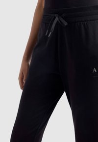 Zwarte jogpants met een geribde tailleband, trekkoordsluiting en logo-detail aan de zijkant; gladde, zachte stof met een relaxte pasvorm.