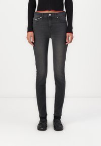 Černé skinny džíny s vybledlým vzhledem, které mají pět kapsičkový design a stříbrné doplňky. Kombinováno s černým pleteným topem a černou obuví.