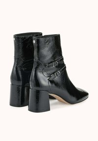 Bottes basses noires brillantes avec talons carrés, sangles latérales à boucle et surface texturée, vues de dos et de côté.