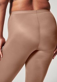 Tan leggings med jevn tekstur og ribbet design. Høy midje og tettsittende silhuett som fremhever en sømløs bakside.
