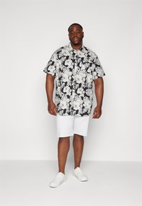 Camicetta floreale bianca e nera a maniche corte abbinata a pantaloni corti bianchi e sneakers bianche. La camicia presenta un motivo tropicale e un design con bottone davanti.