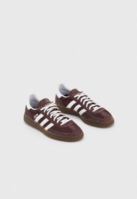 Sneakers in pelle scamosciata marrone con strisce bianche, suola in gomma e lacci bianchi. Include un collo imbottito e una punta testurizzata.