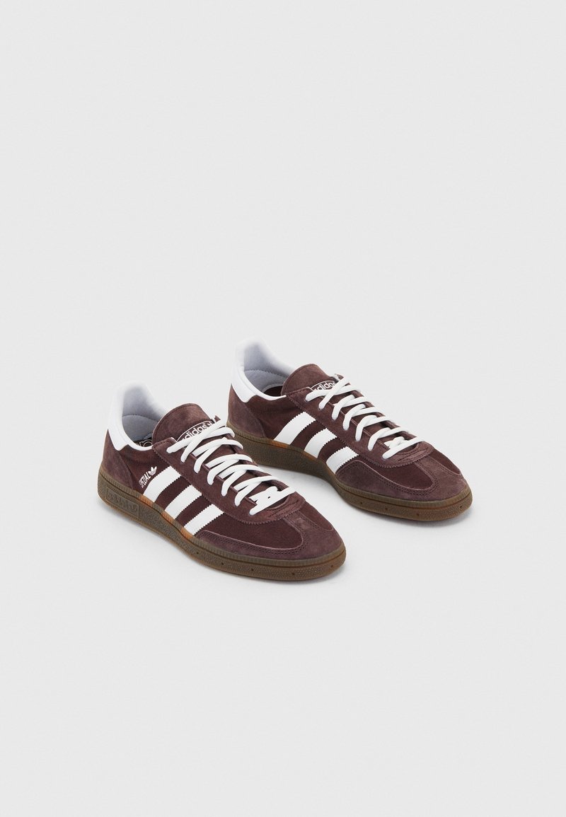 Sneakers in pelle scamosciata marrone con strisce bianche, suola in gomma e lacci bianchi. Include un collo imbottito e una punta testurizzata.
