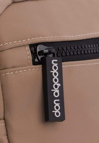 Bolsa de tela beige con un cierre negro, que presenta una etiqueta rectangular con "don diadorn" en texto blanco, destacando detalles del material y diseño.
