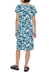 Robe fleurie avec un motif teal et blanc, manches courtes, coupe décontractée, longueur genoux, associée à des sandales noires.