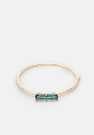 Goldfarbener Armreif mit einem rechteckigen blauen Kristall-Mittelstück, dargestellt auf weißem Hintergrund.
