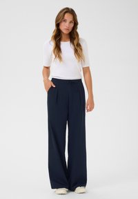 Marineblaue weite Hosen mit einem Kordelzugbund und seitlichen Taschen, kombiniert mit einem schmal geschnittenen weißen Kurzarmoberteil. Glatte Stofftextur.