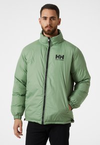Pufferjack in lichtgroen met een hoge kraag, ritssluiting, elastische manchetten en zwart logo-detail op de borst. Glad, glanzend textuur.