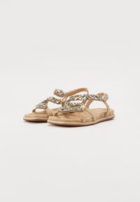 Beige sandaler med en knyttet design, prydet med flerfargede rhinestones. Mykt semsket skinnmateriale og flat såle med glitrende kant.