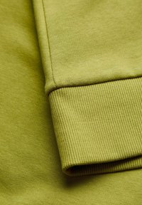 Green cotton fabric showcasing a smooth texture, with a ribbed cuff detail. The fabric is slightly stretchable and uniform in color.