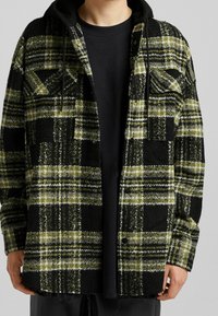 Svart och grön rutig flanelljacka med luva, med knäppning framtill, två bröstfickor och strukturerad tyg med en något upprepad nederkant.