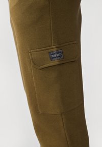 Olivgrüne Jogginghosen aus einem weichen Baumwollmischgewebe. Mit einer Seitentasche mit einem Etikett der Marke "Pier One". Enganliegendes Design.