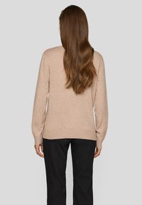 Beiger Strickpullover mit langen Ärmeln, lockerem Schnitt und gerippten Bündchen sowie Saum, kombiniert mit schwarzen Hosen.