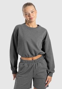 Felpa grigia a maniche lunghe con orlo elastico abbinata a pantaloni corti, caratterizzata da un logo ricamato e una vestibilità rilassata.