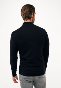 Černé polo tričko s dlouhým rukávem a žebrovaným límcem a manžetami, vyrobené z hladkého materiálu, spárováno s světle šedými džínami.