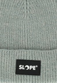 Vaaleanharmaa neulottu pipomalli, jossa on ribbikuvio. Mustassa suorakulmaisessa tarrassa lukee valkoisella tekstillä "SLOPE". Pehmeä rakenne.