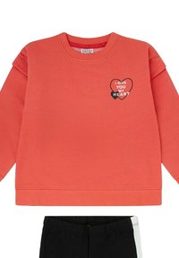 Sudadera coral de manga larga con dos gráficos de corazones y texto "TE DOY MI CORAZÓN" en el pecho, combinada con pantalones negros con una franja blanca.