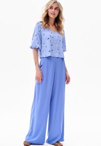 Lichtblauwe bloemenblouse met korte mouwen, gecombineerd met wijde broek in een bijpassende blauw tint. Glad materiaal met een ontspannen pasvorm.