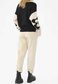 Pull en maille noir et crème avec un motif abstrait sur les manches, associé à un pantalon crème taille haute et des bottines noires à lacets.