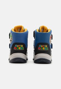 Baskets montantes bleues avec doublure jaune, accents noirs et patches de personnages de Super Mario. Bandes Velcro pour la fermeture ; semelle en caoutchouc.