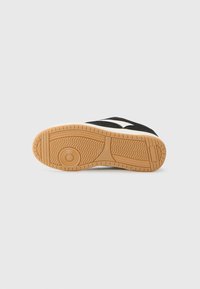 Black sneaker sole with a textured gum rubber outsole, featuring a wavy pattern and grooves for traction. Minimalist design, durable material.