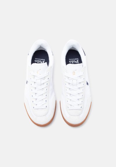 Hvite joggesko laget av lær og stoff, med gummisåle, rund tupp, flate lisser og en marineblå logo på tungen.