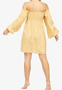 El vestido amarillo sin mangas presenta un cuerpo fruncido y mangas abullonadas, adornado con pequeños patrones florales en todo su diseño.