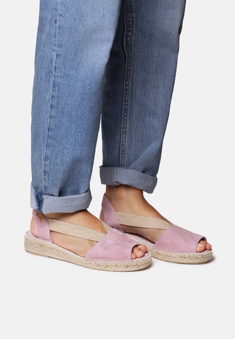 Rožnate semiš espadrile z odprto konico, elastičnimi čezkrvnimi trakovi in pletenim juto podplatom. Ujemajo se s sploščeni jeans hlačami.