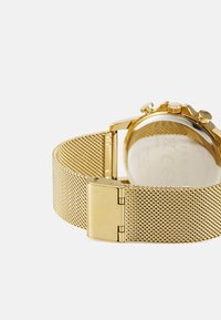Montre avec bracelet en maille dorée, boîtier rond poli et fond en verre. Elle dispose de plusieurs boutons sur le cadran et d'un fermoir métallique sécurisé.
