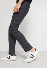 Pantaloni grigi scuri realizzati in tessuto testurizzato, design slim fit con una tasca posteriore, abbinati a sneakers bianche con accenti neri.