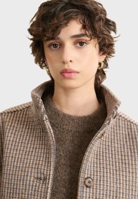 Brown plaid wool jacket with a collared neckline, featuring a button closure and textured brown sweater underneath.