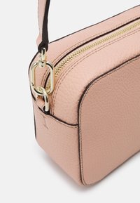 Růžová kožená crossbody taška s hladkou strukturou, zlatým zipem a pečlivým prošíváním podél okrajů. Má odnímatelný popruh.