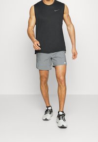 Svart ärmlös Nike-topp, grå shorts med sidofickor, vitt Nike-logotyp, och svartvita träningsskor. Slät tygstruktur.