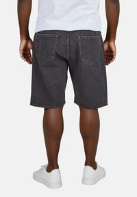 Pantalones cortos de mezclilla negra de corte recto, con dos bolsillos traseros y una textura ligeramente desgastada. Combinados con zapatillas blancas.