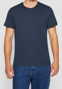 Navy blue cotton T-shirt with short sleeves, round neckline, and a small logo on the left chest. Smooth texture, standard fit.