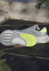 Baskets de sport grises avec une tige en maille texturée, accents jaune fluo, et une semelle intermédiaire blanche dotée d'une semelle en caoutchouc à motifs pour l'adhérence.