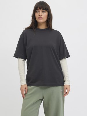 Zwarte korte mouwen t-shirt van katoen, met een ontspannen pasvorm, gelaagd over een lichtgrijze longsleeve top, gecombineerd met groene broek.