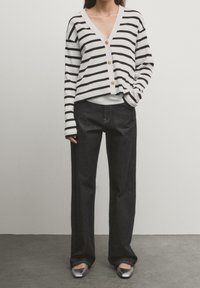 Black and white striped cropped cardigan with gold buttons, paired with dark wide-leg jeans and silver flats. Smooth fabric and loose fit.